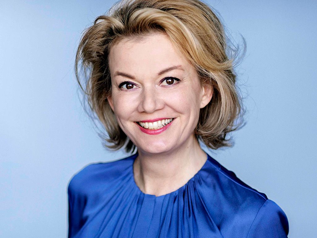 Preview of: Smilende kvinde med kort blondt hår og blå bluse mod en lyseblå baggrund