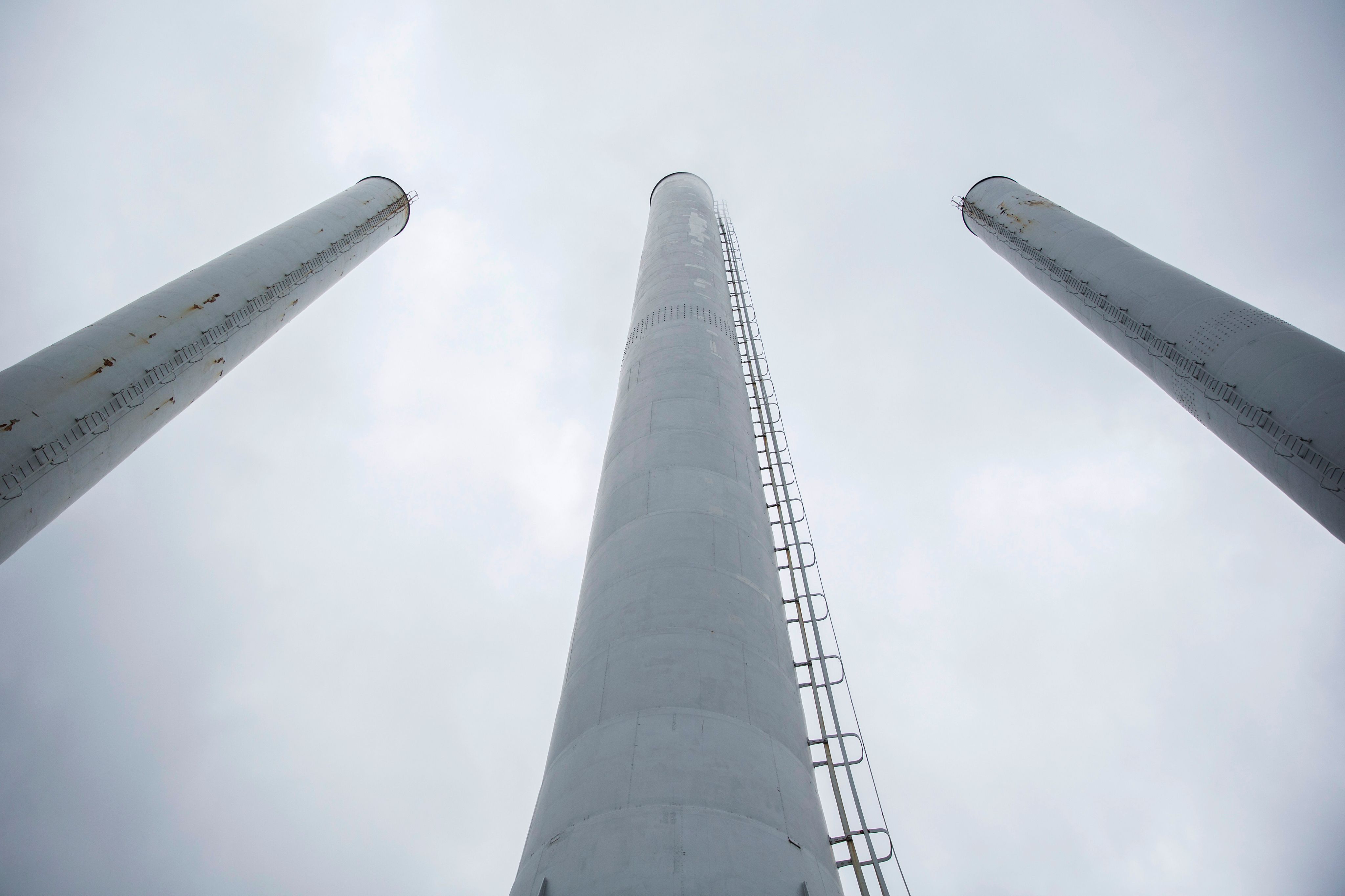 Preview of: Tre høje, hvide skorstene set nedefra mod en overskyet himmel