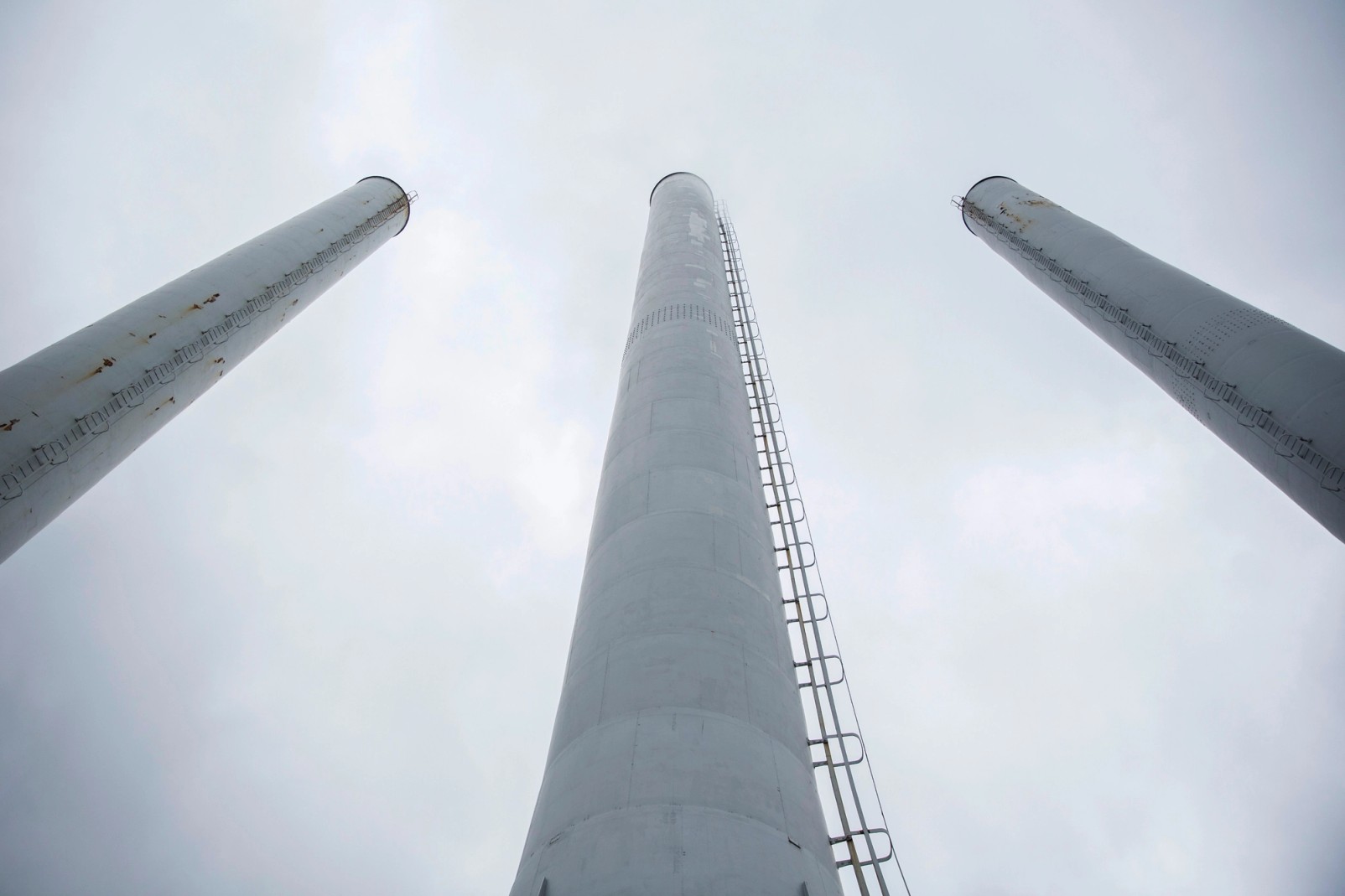 Tre høje, hvide skorstene set nedefra mod en overskyet himmel