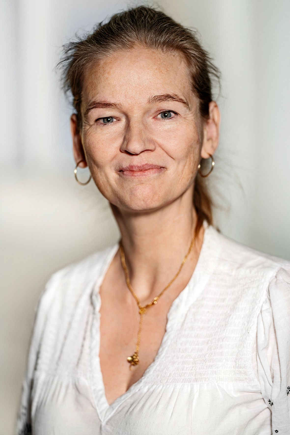Preview of: Smilende kvinde med opsat hår, hvid bluse, guldsmykke og ringøreringe