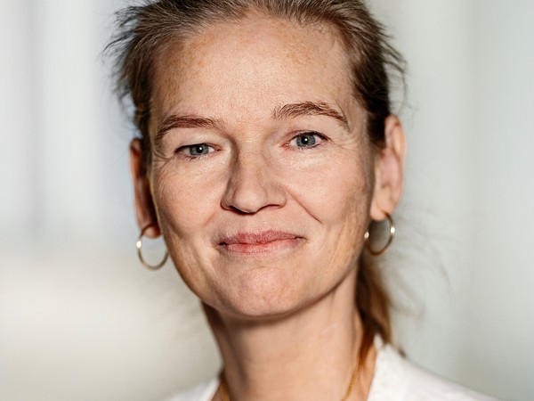Smilende kvinde med opsat hår, hvid bluse, guldsmykke og ringøreringe