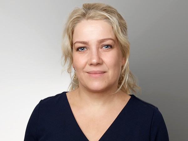 Portræt af en blond kvinde i mørkeblå bluse mod en grå baggrund