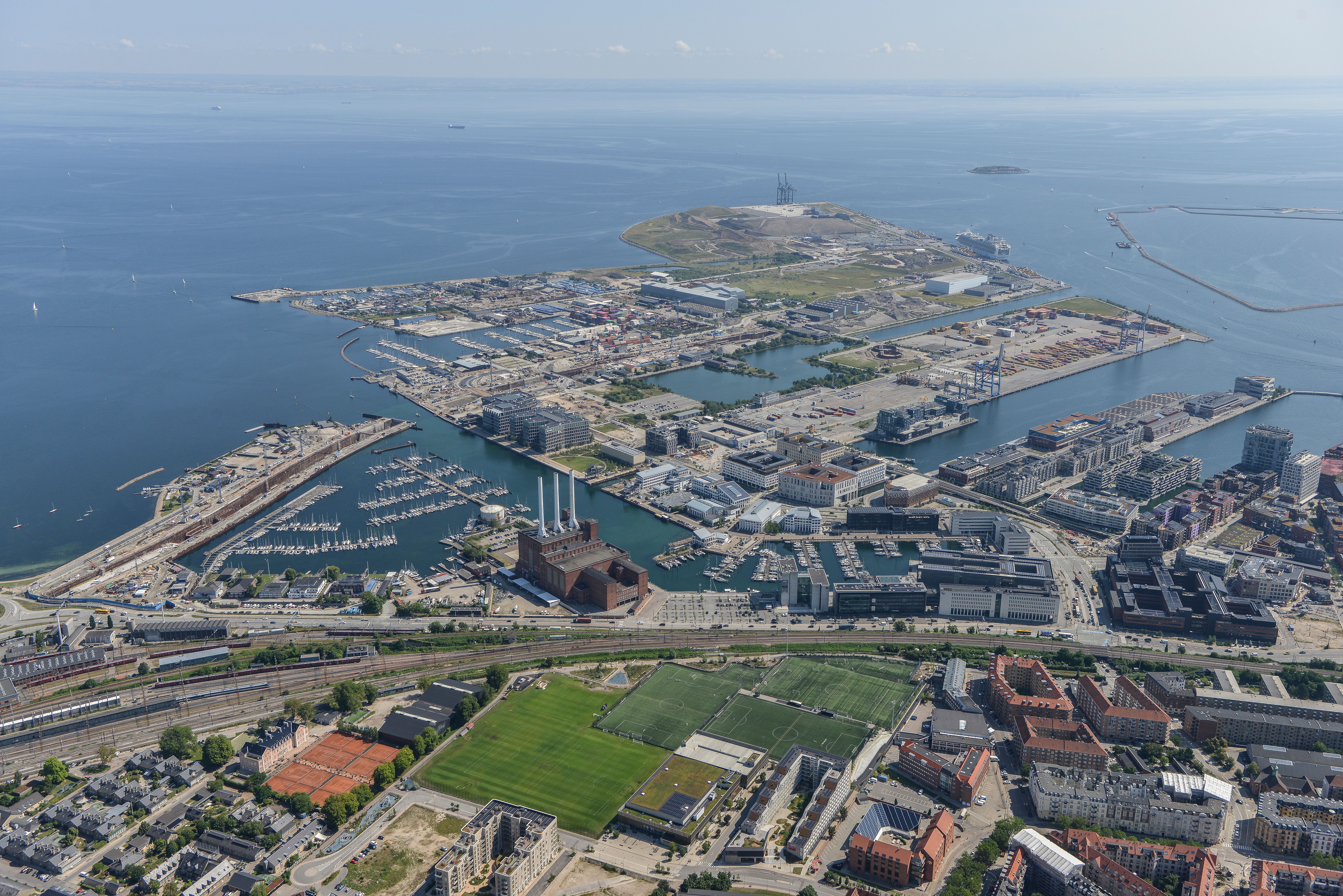 Preview of: Luftudsigt over havneområde med marinaer, bygninger, jernbane og fodboldbaner