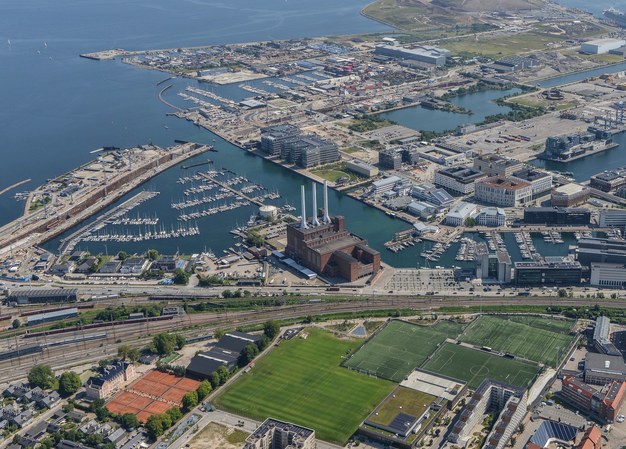 Luftudsigt over havneområde med marinaer, bygninger, jernbane og fodboldbaner