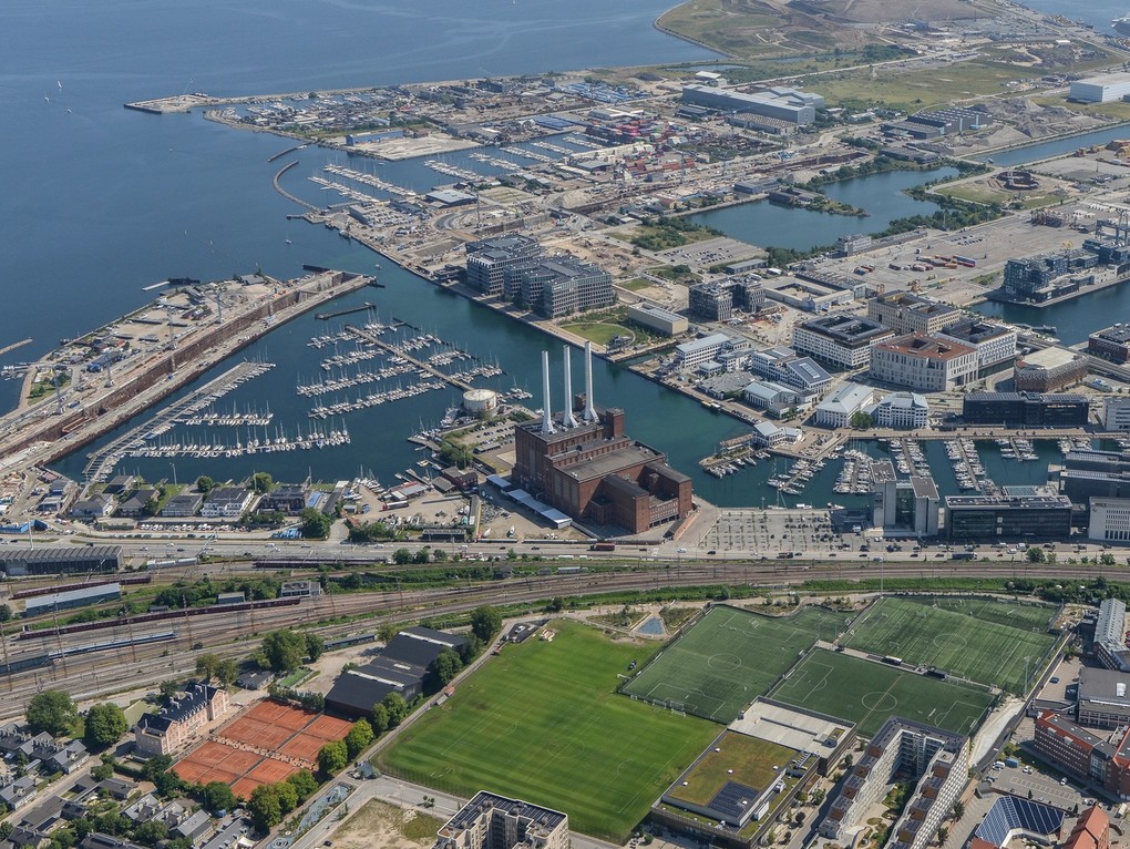 Luftudsigt over havneområde med marinaer, bygninger, jernbane og fodboldbaner