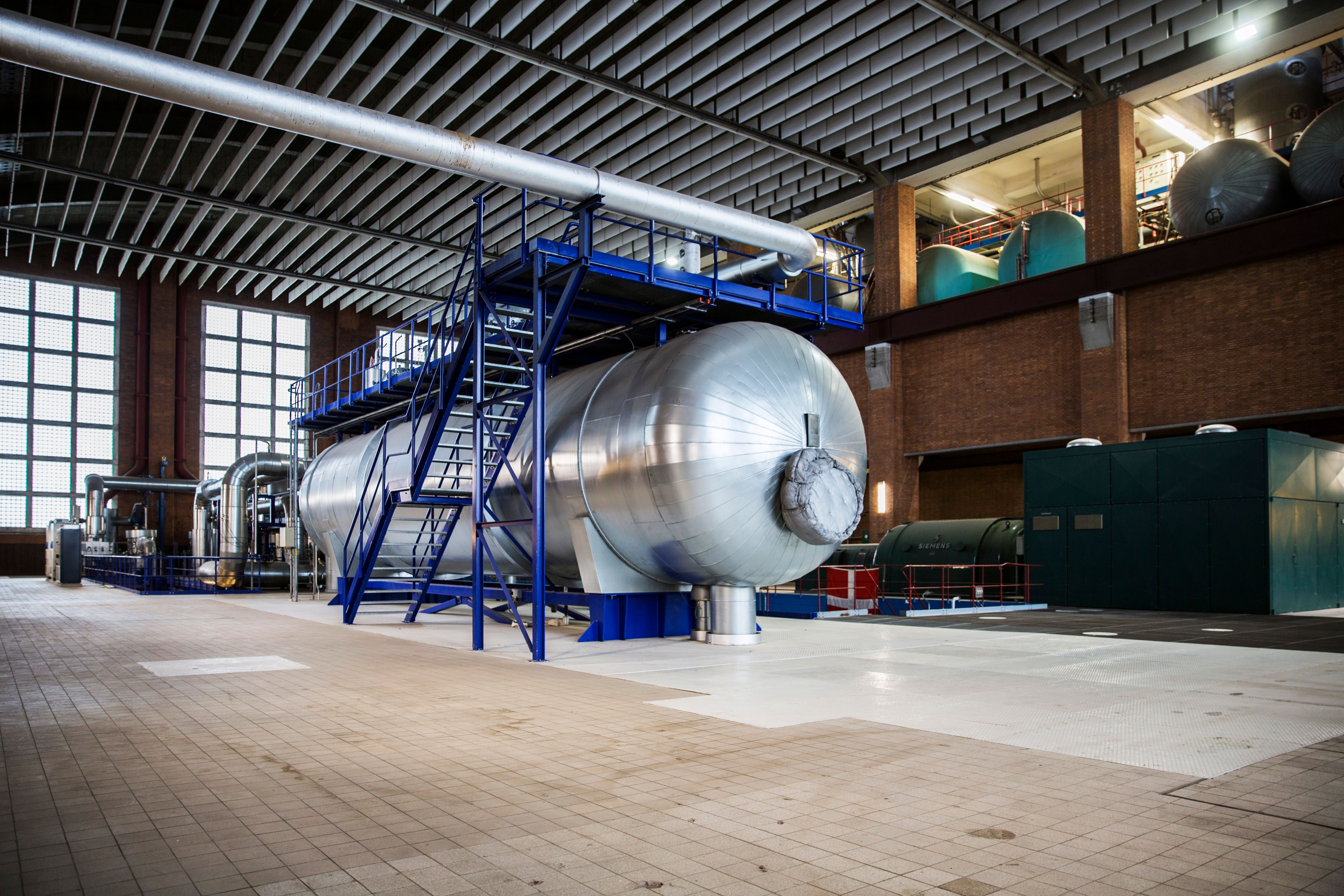 Preview of: Stor cylindrisk ståltank med blå trapper og rør i en industrihal
