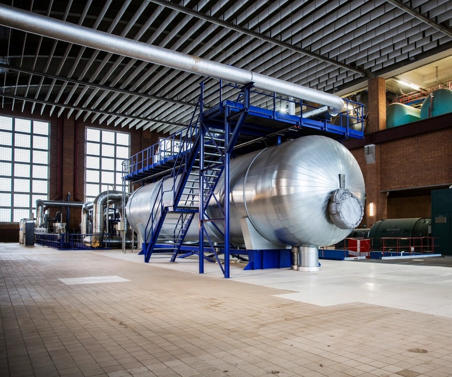 Stor cylindrisk ståltank med blå trapper og rør i en industrihal