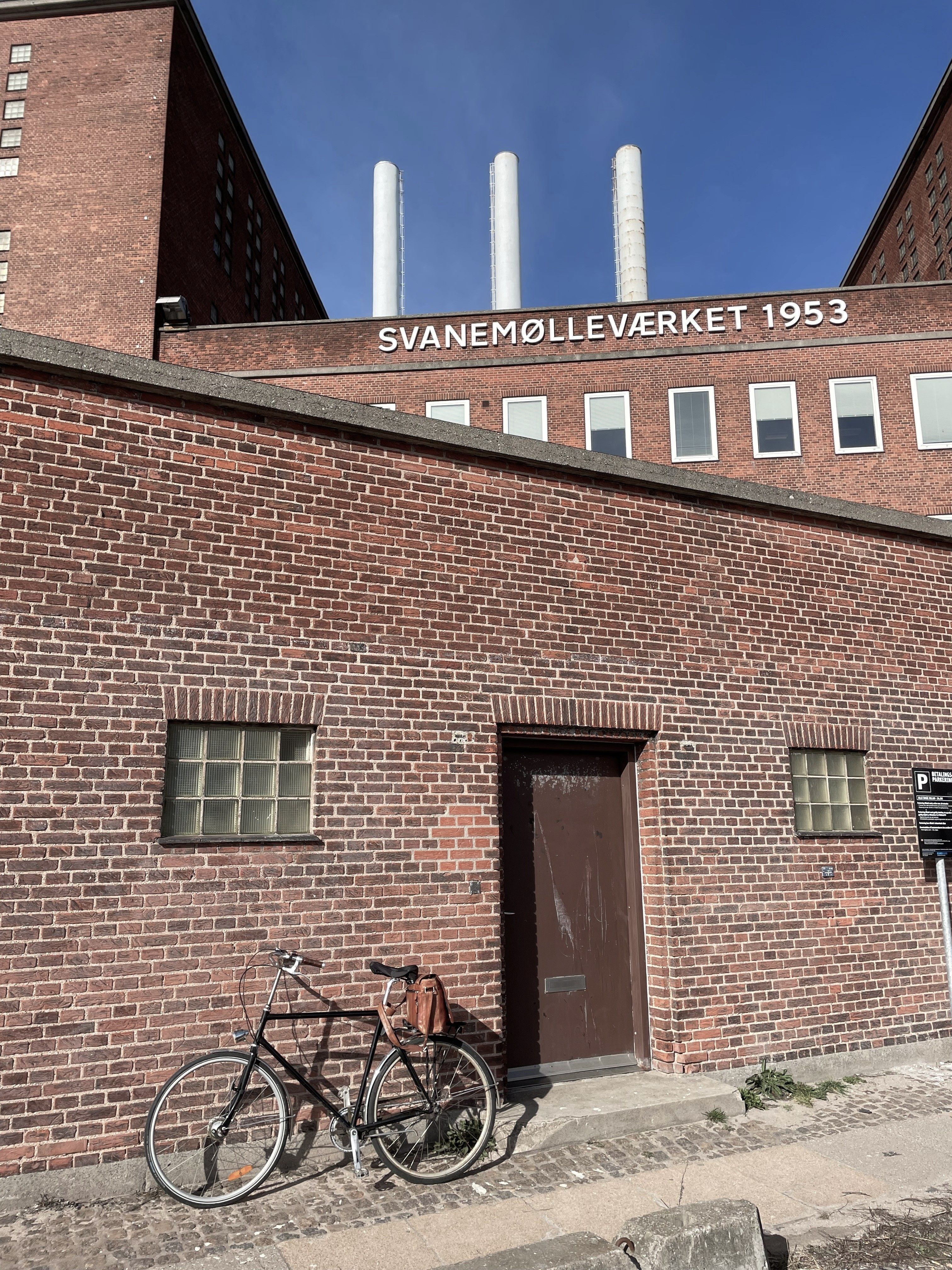 Preview of: Rød murstensbygning ved Svanemølleværket med cykel og tre skorstene