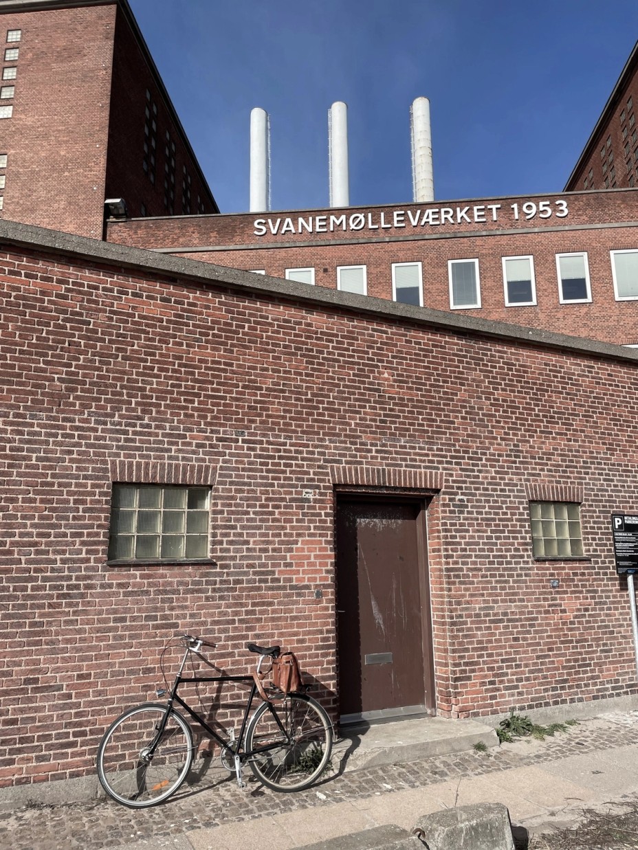 Rød murstensbygning ved Svanemølleværket med cykel og tre skorstene