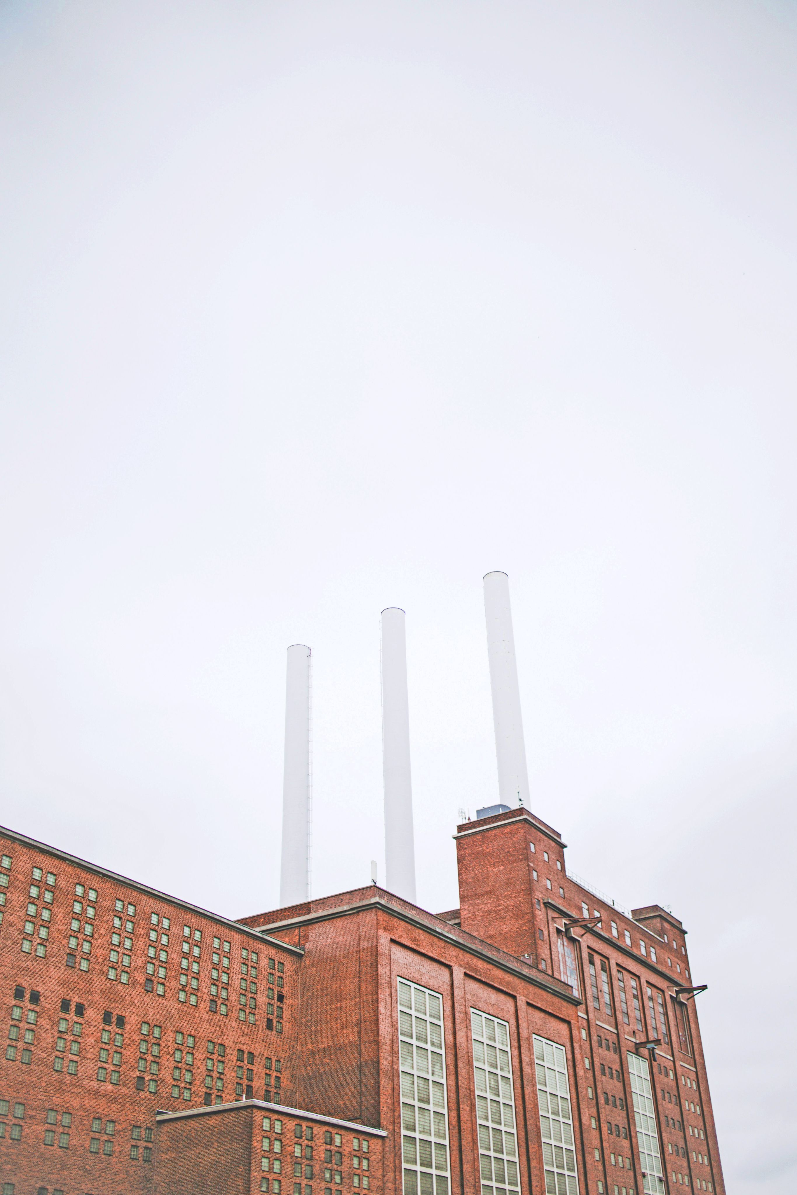Preview of: Rød industribygning i mursten med tre høje, hvide skorstene under en overskyet himmel