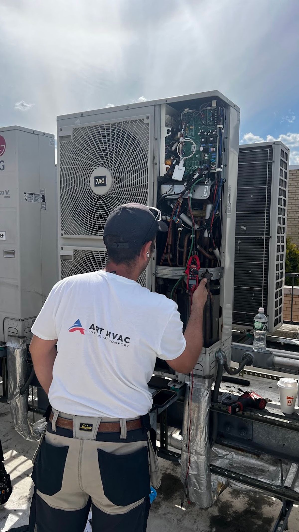 Art HVAC technician testing an opened heat pump outdoor unit with a clamp meter on a rooftop in New York