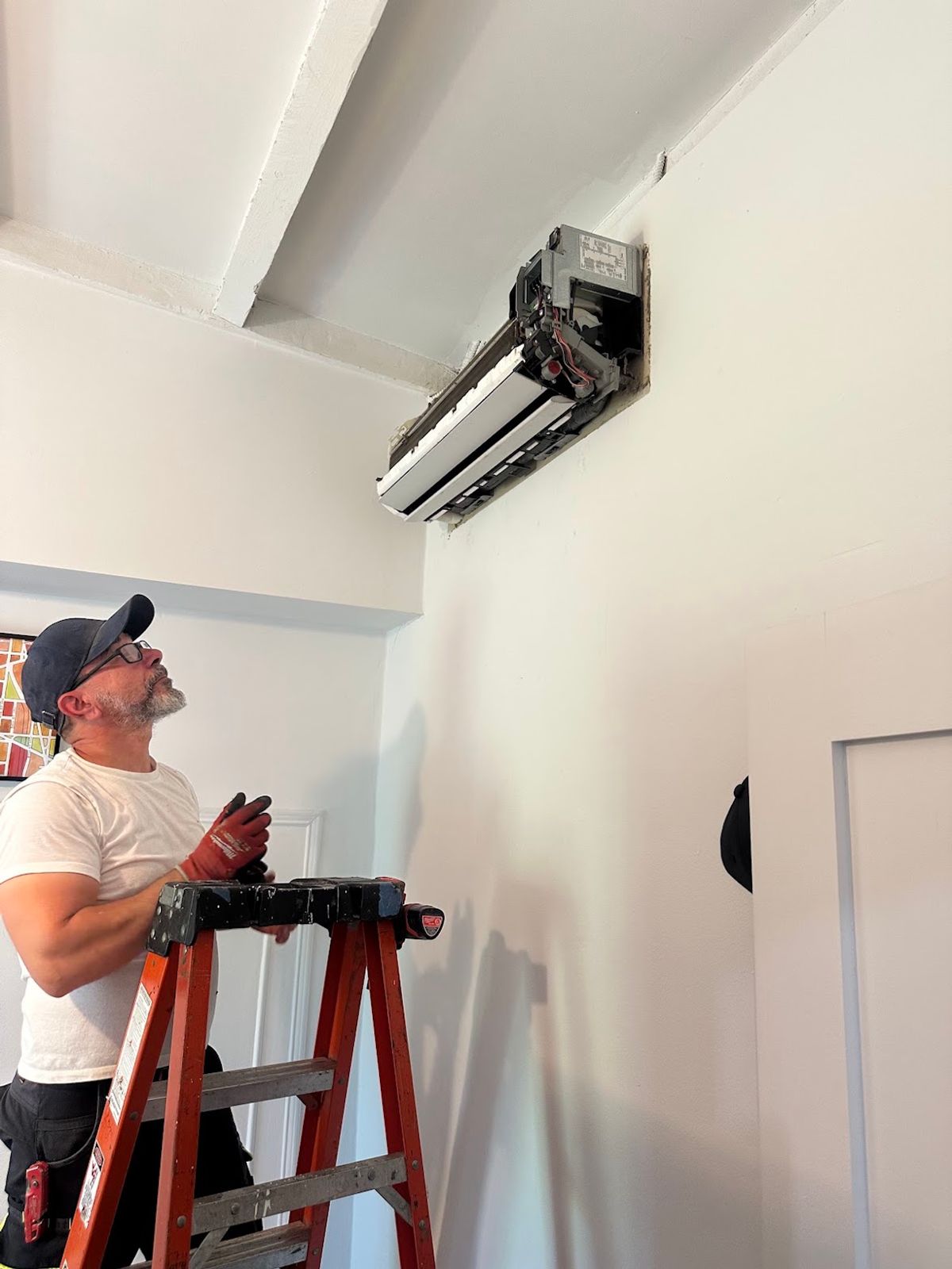 Art HVAC installer on a ladder mounting a ductless mini-split wall unit in a New York City apartment