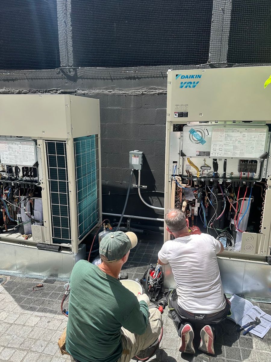 Two Art HVAC technicians commissioning Daikin outdoor units with the panels removed on a Brooklyn rooftop