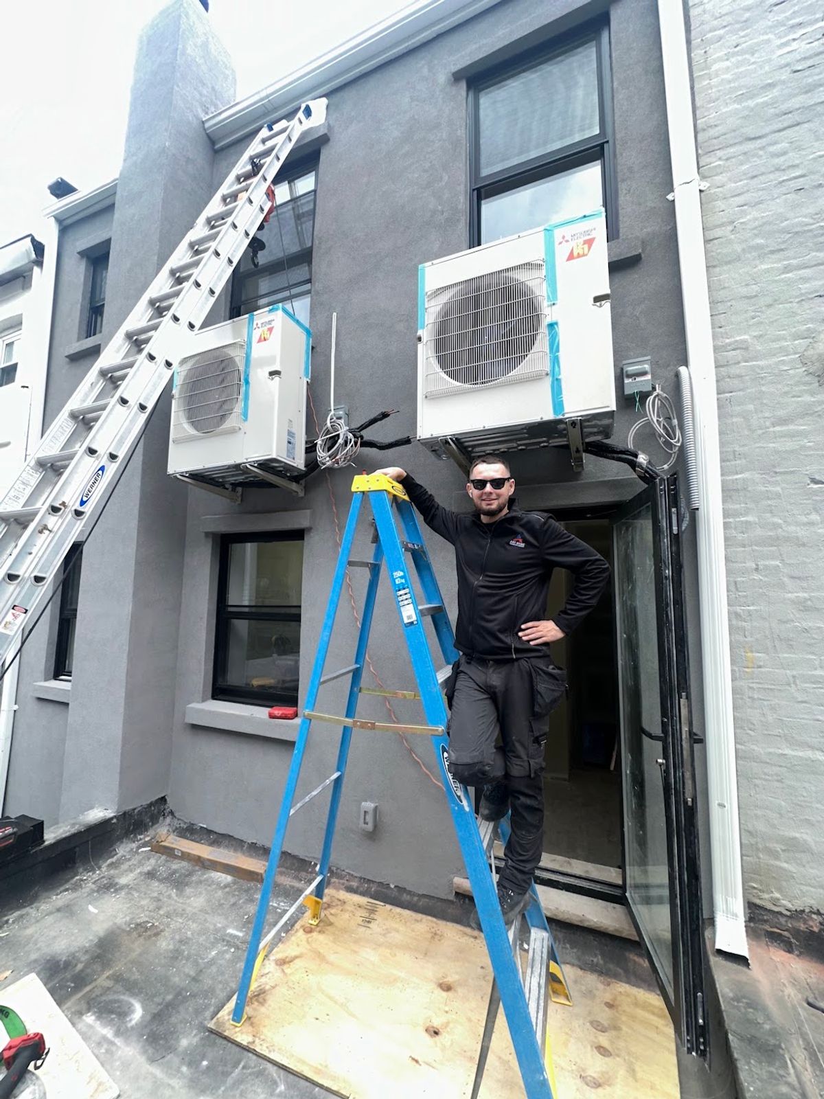 Two Mitsubishi cold-climate heat pump outdoor units wall-mounted on the rear elevation of a New York City building during a ductless installation