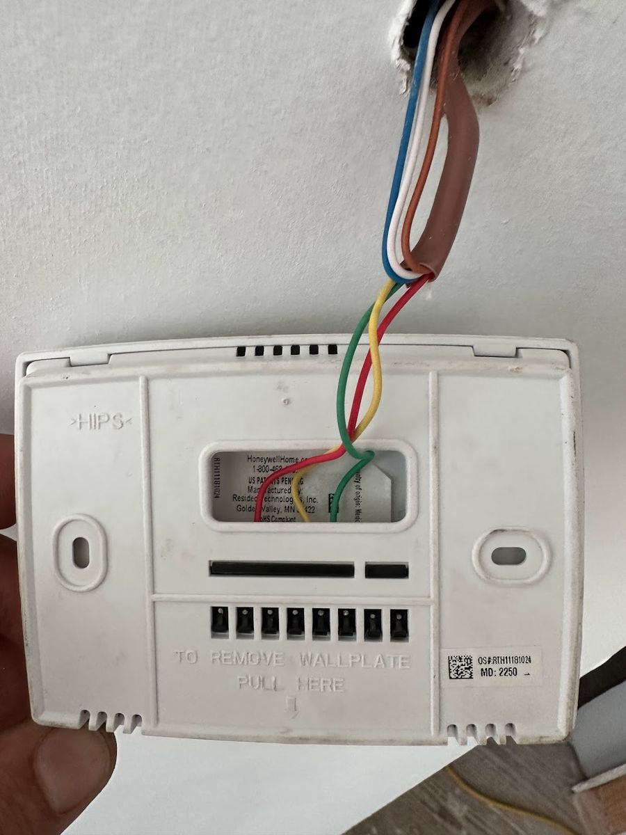 Thermostat wallplate removed from the wall showing the labeled wire terminals during a heating diagnosis