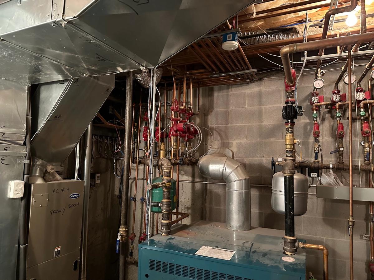 Apartment building boiler room in New York City with a cast-iron boiler, flue pipe and zone piping, ready for heat season