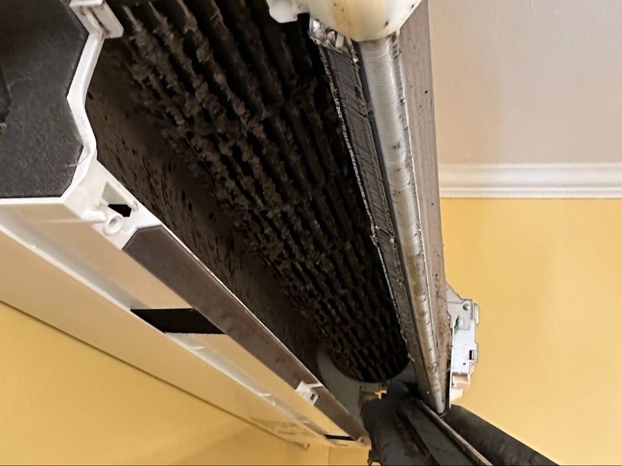 Wall-mounted mini-split opened up to show a blower wheel and indoor coil caked with dirt behind the filters