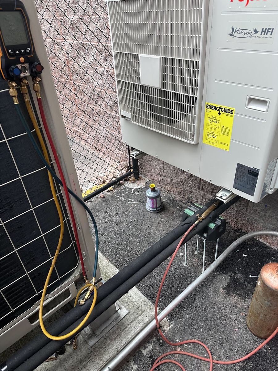 EnergyGuide efficiency label on a heat pump outdoor unit, with manifold gauges connected during a service visit