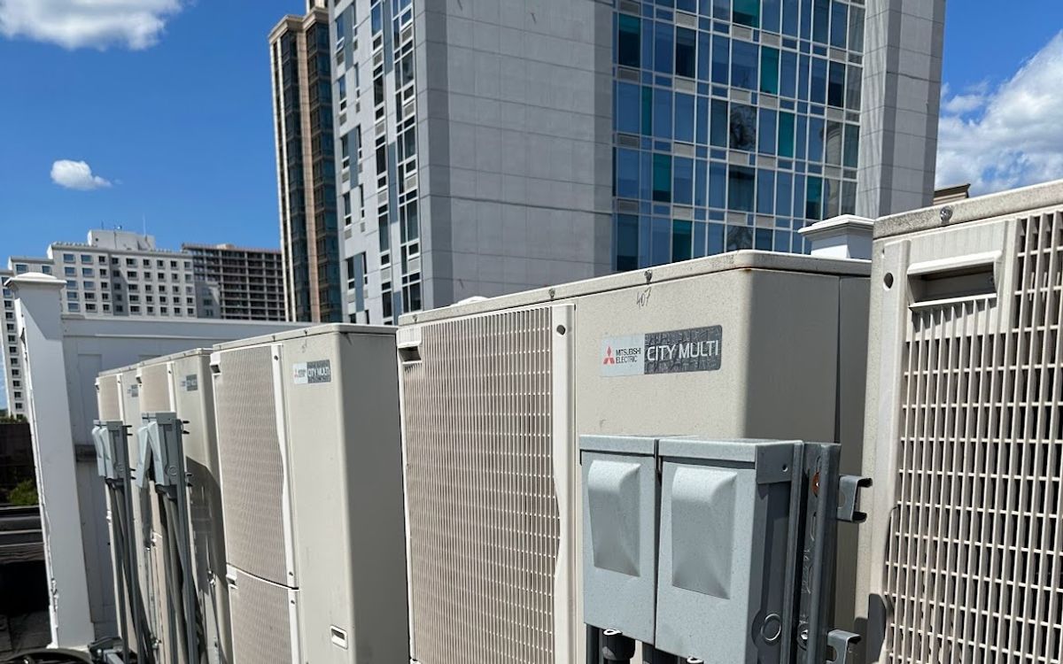 Row of Mitsubishi Electric City Multi heat pump outdoor units on a New York rooftop, with high-rise towers behind
