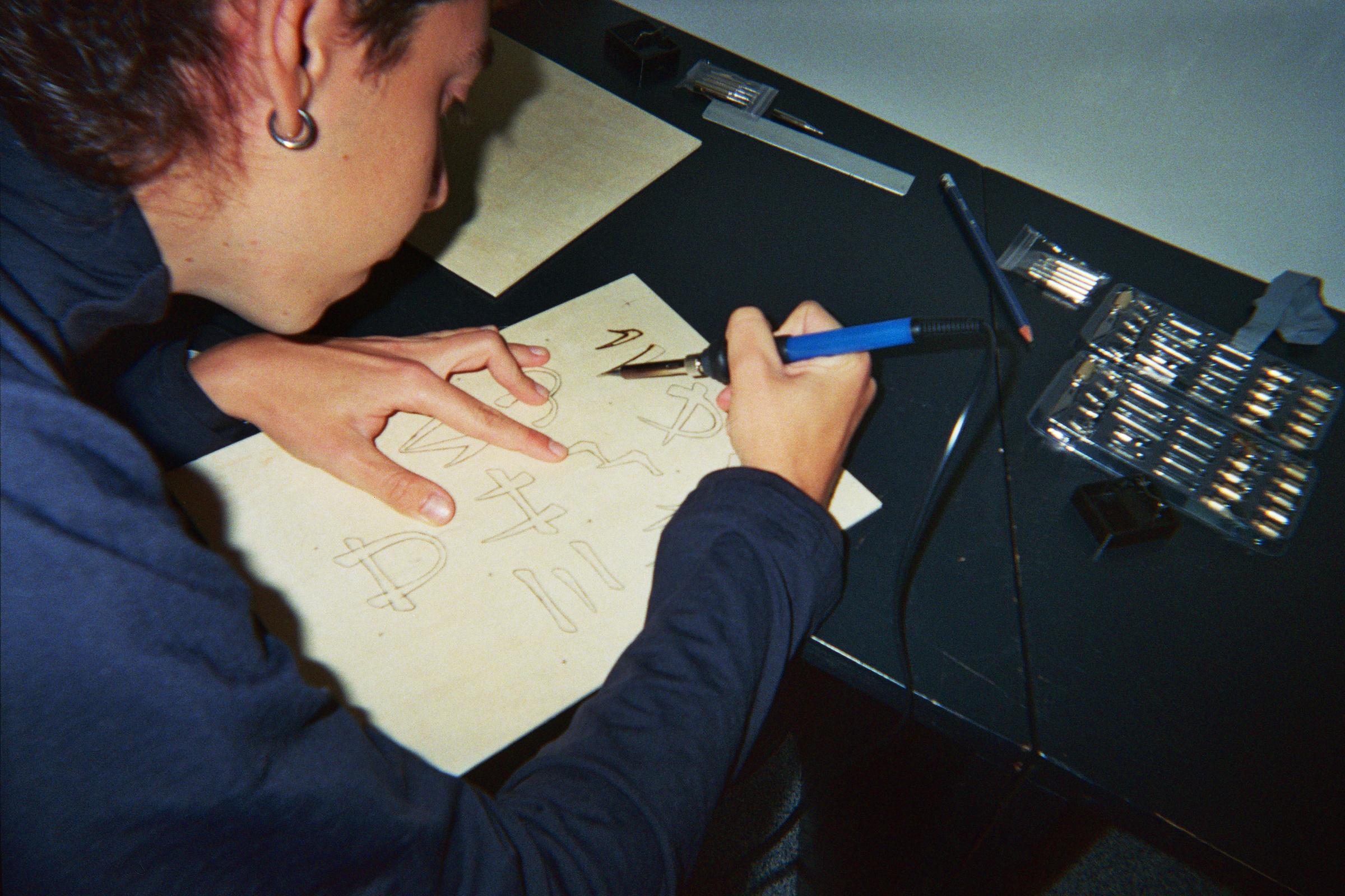 Participant engraving glyph sketches onto a wooden panel with a pyrography tool.