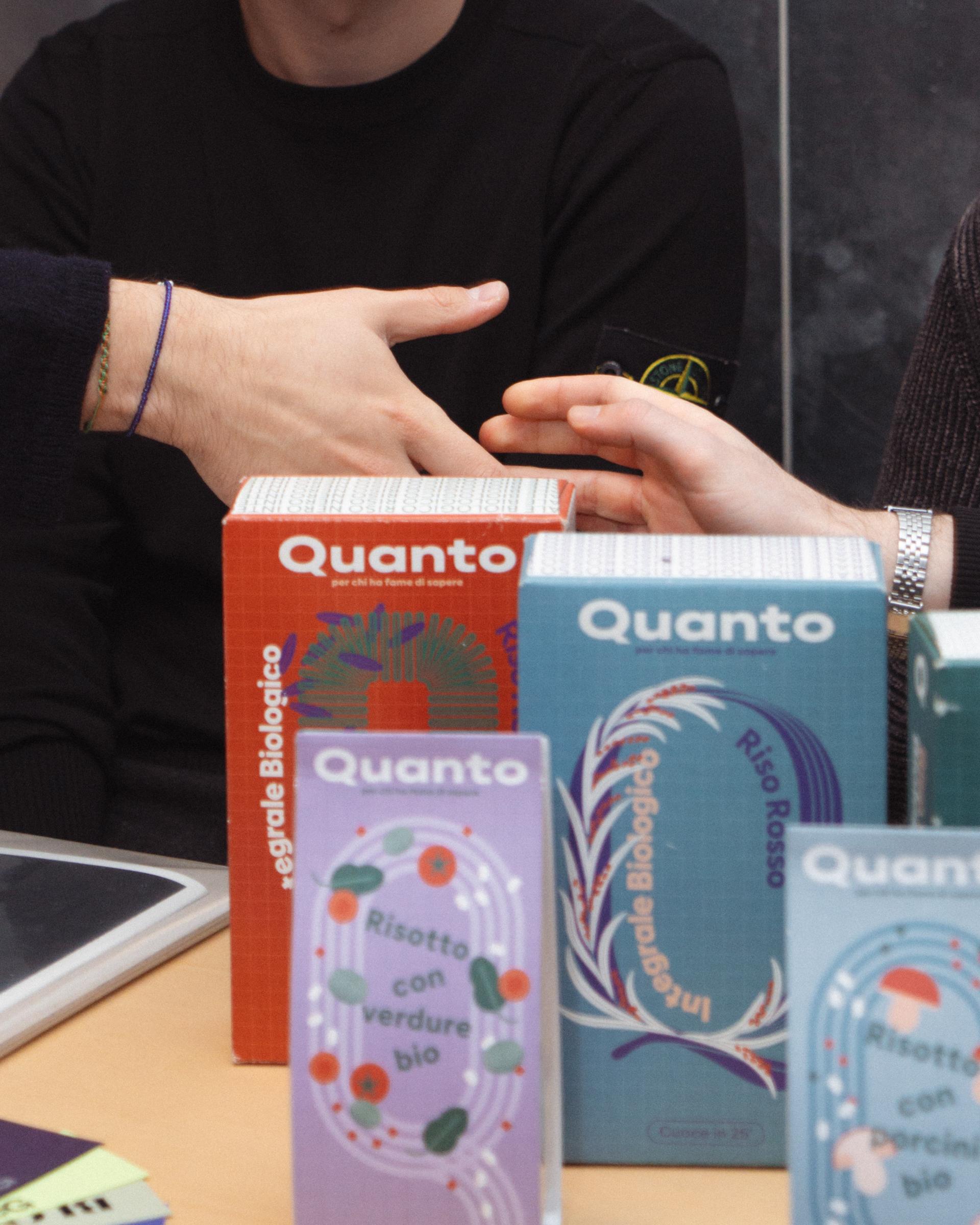 Quanto food boxes and a beer bottle on a table as hands meet in the background.