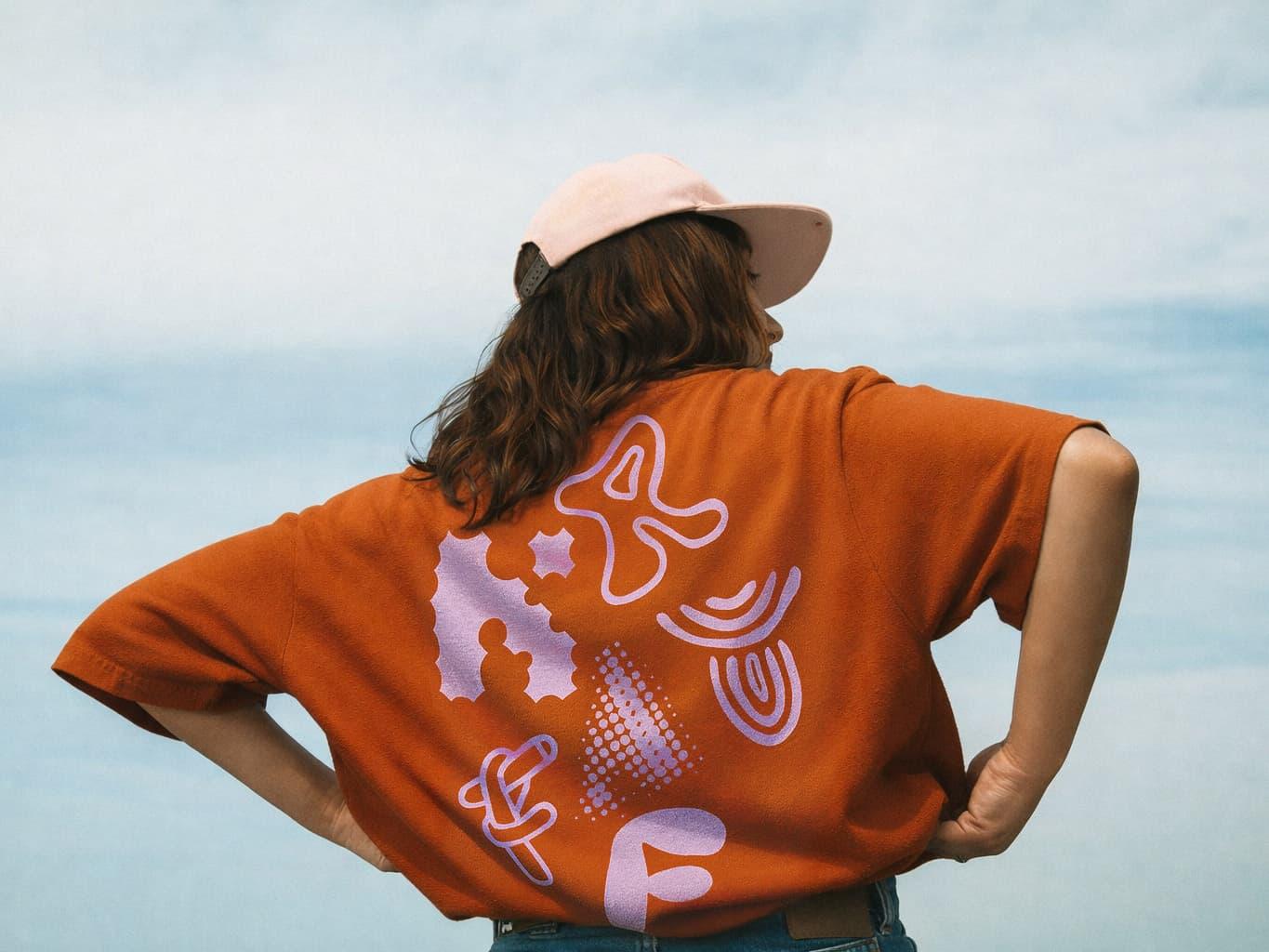 Person wearing an orange Kraftoria T-shirt with purple graphic symbols.