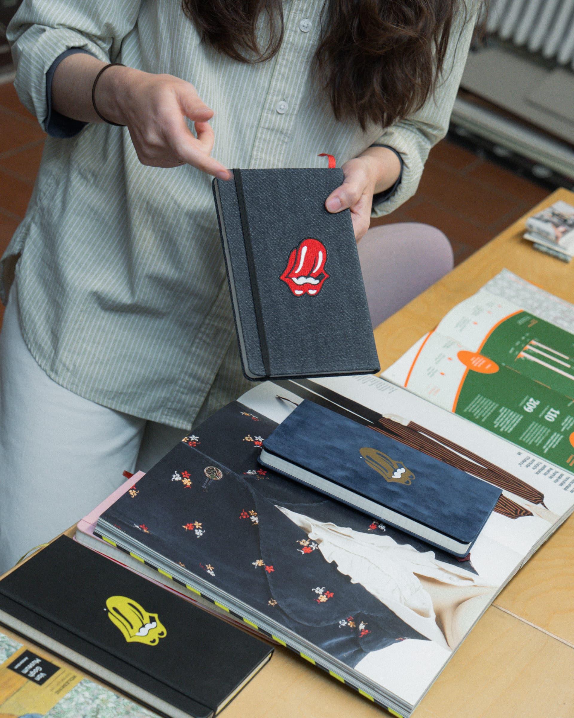 Attendee holding a black notebook with a red embroidered motif above printed materials.