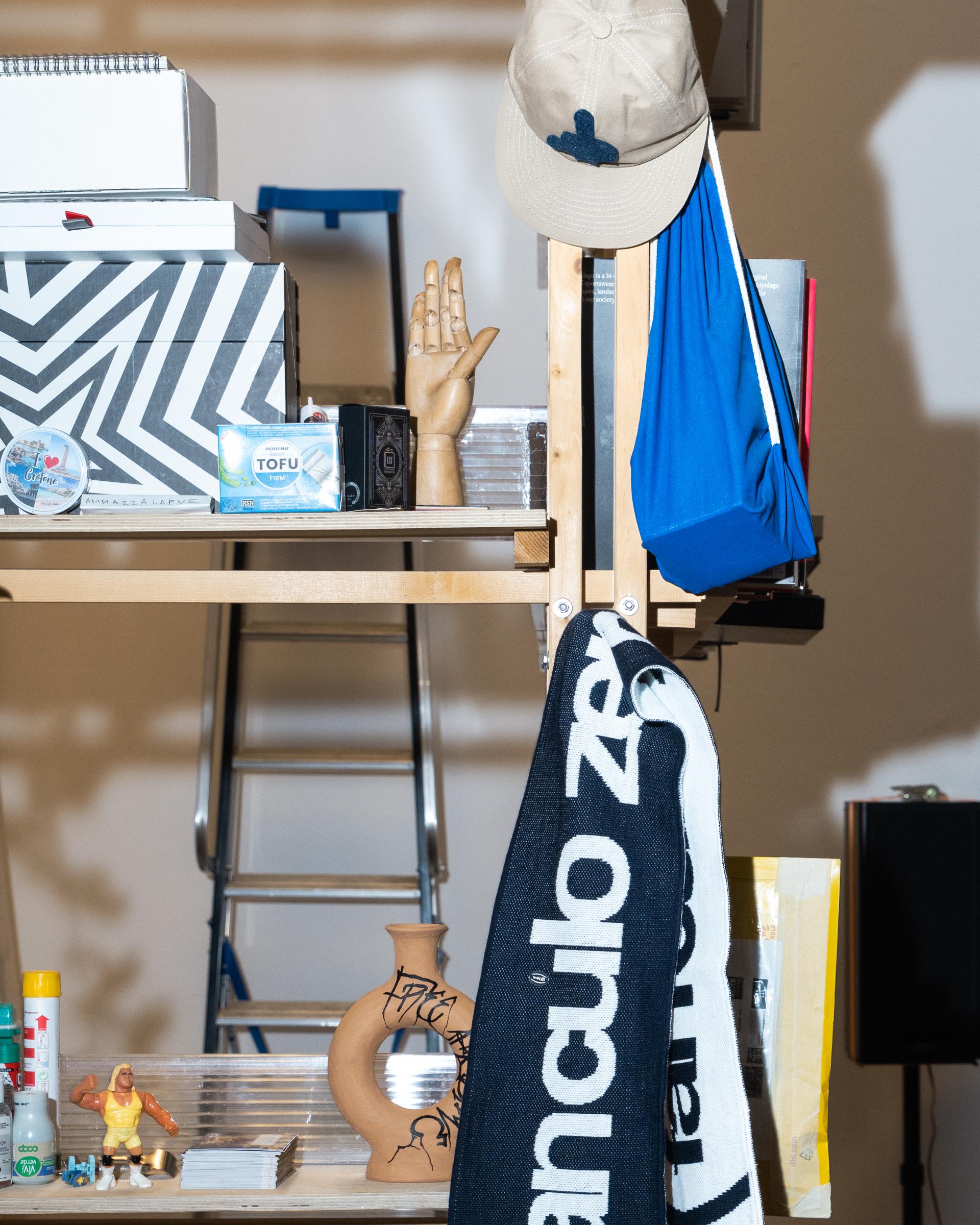 Firm studio shelf with a blue garment, caps, a black-and-white scarf and printed matter.
