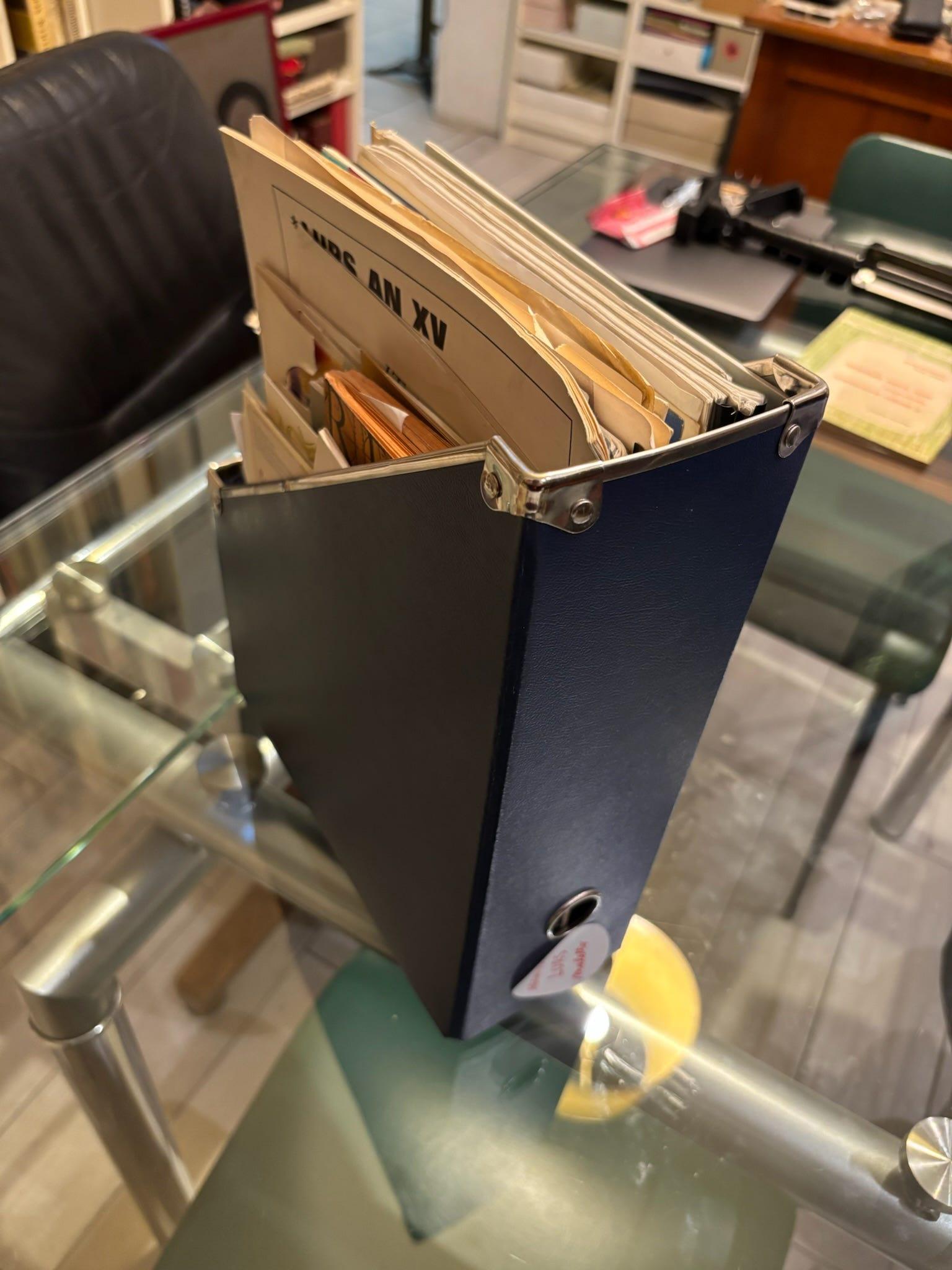 Open blue archive binder filled with paper files on a glass table.