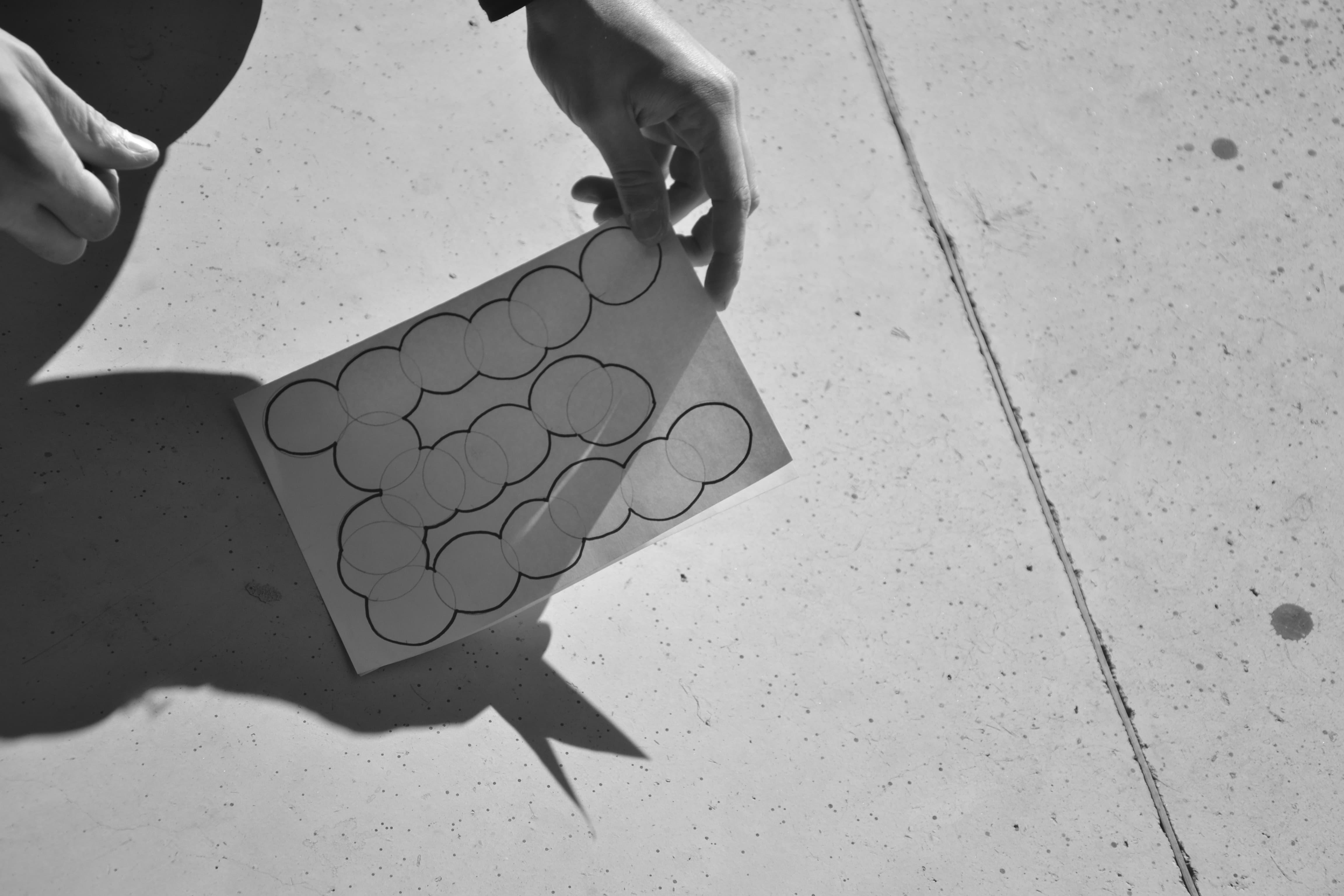 Hand holding a white print with overlapping outlined circles on concrete.