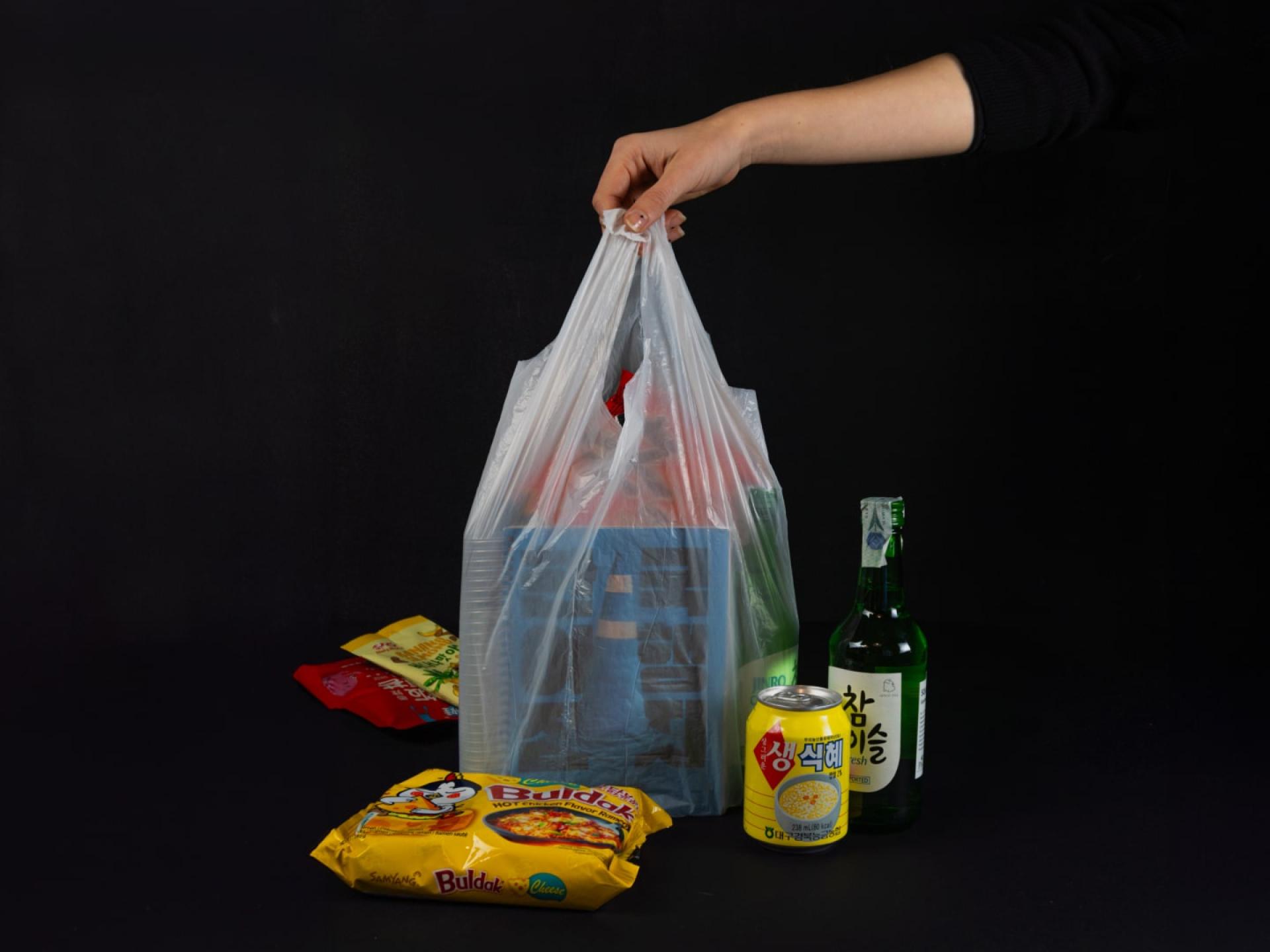 Hand holding a transparent bag with snacks and bottled drinks against black.