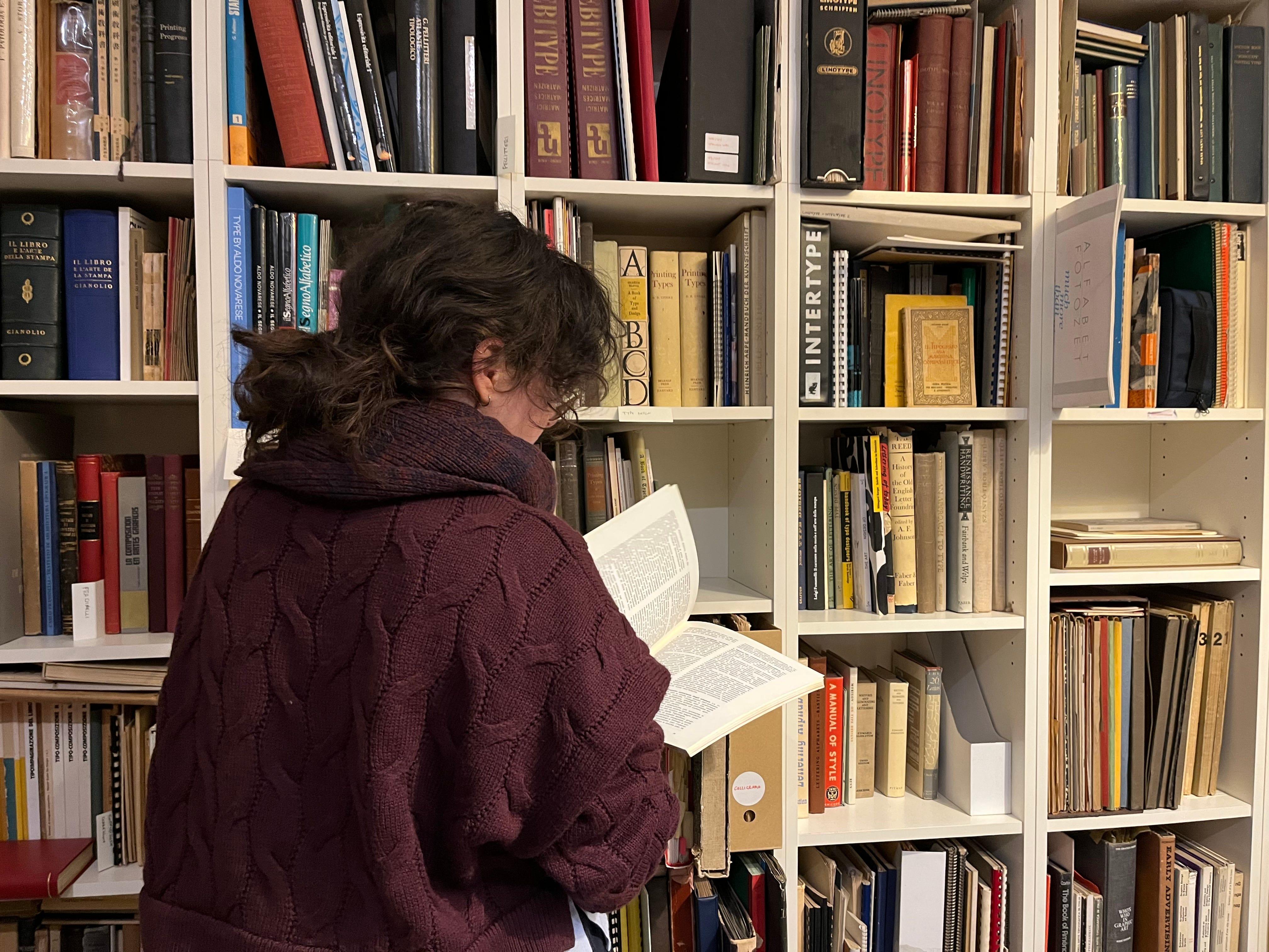 Researcher reading a book in front of shelves at the Library of the Politecnico di Torino.