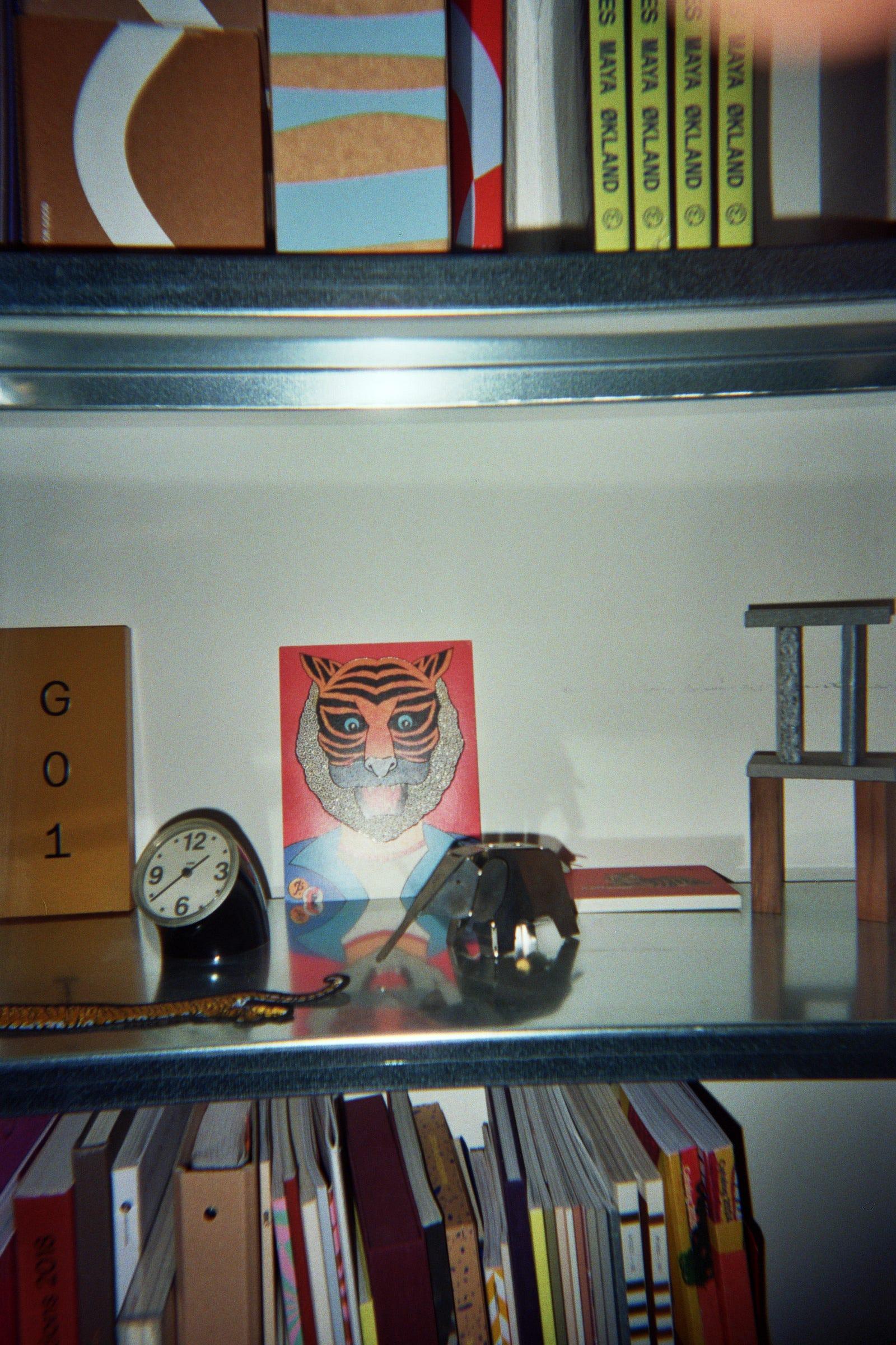 Studio shelf with a tiger illustration, clock, small sculptures and books.
