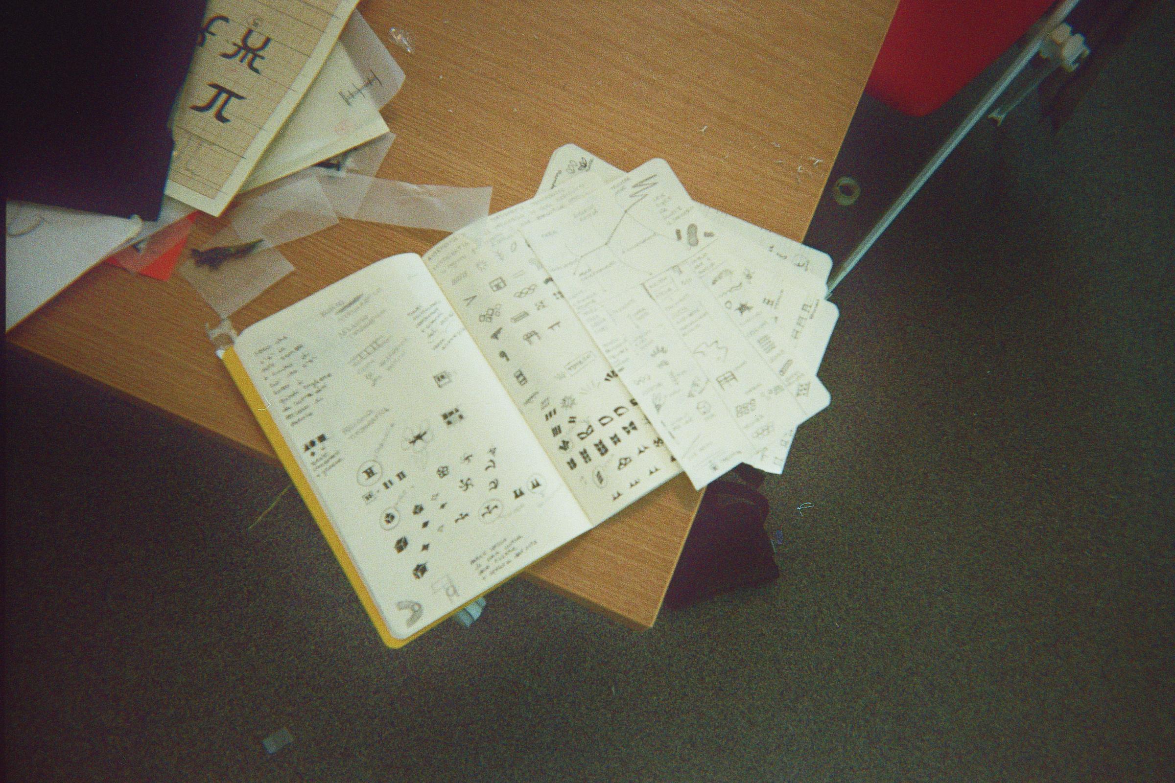 Open notebook and loose sheets of glyph sketches on a workshop table.