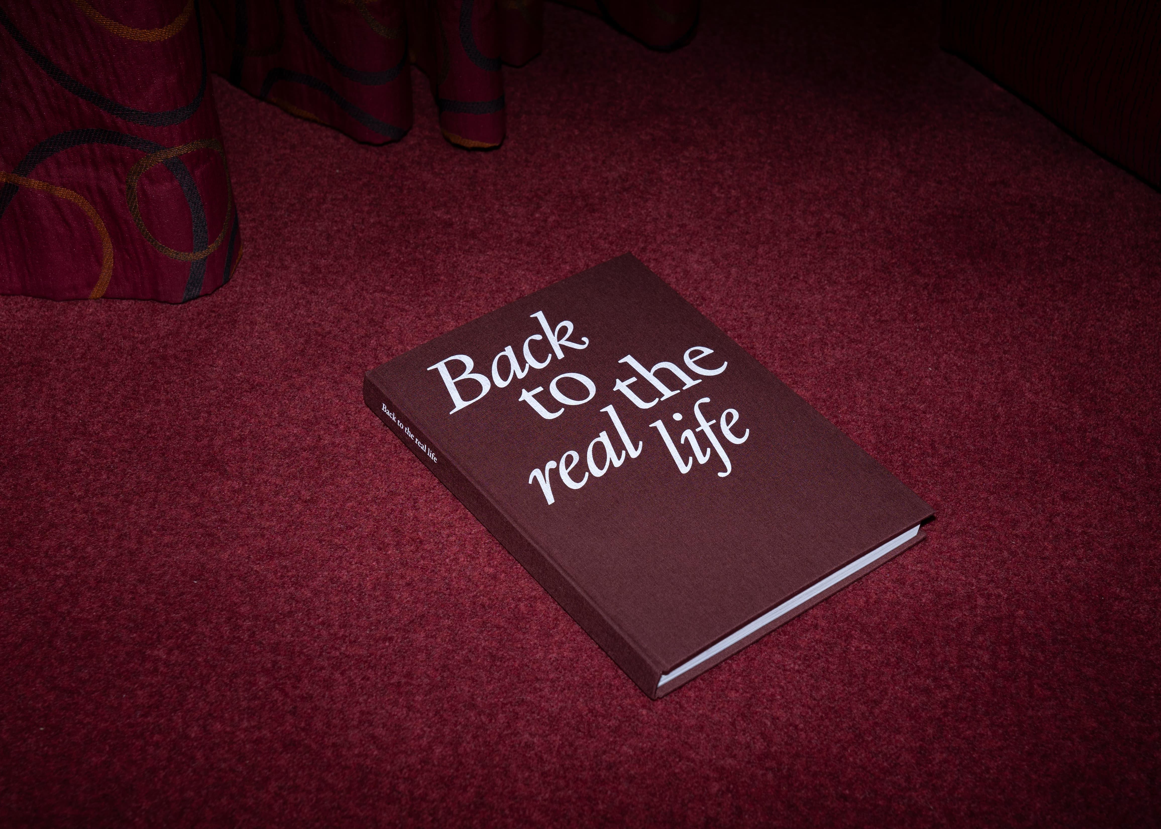 Dark red Back to the real life book on a red carpet.