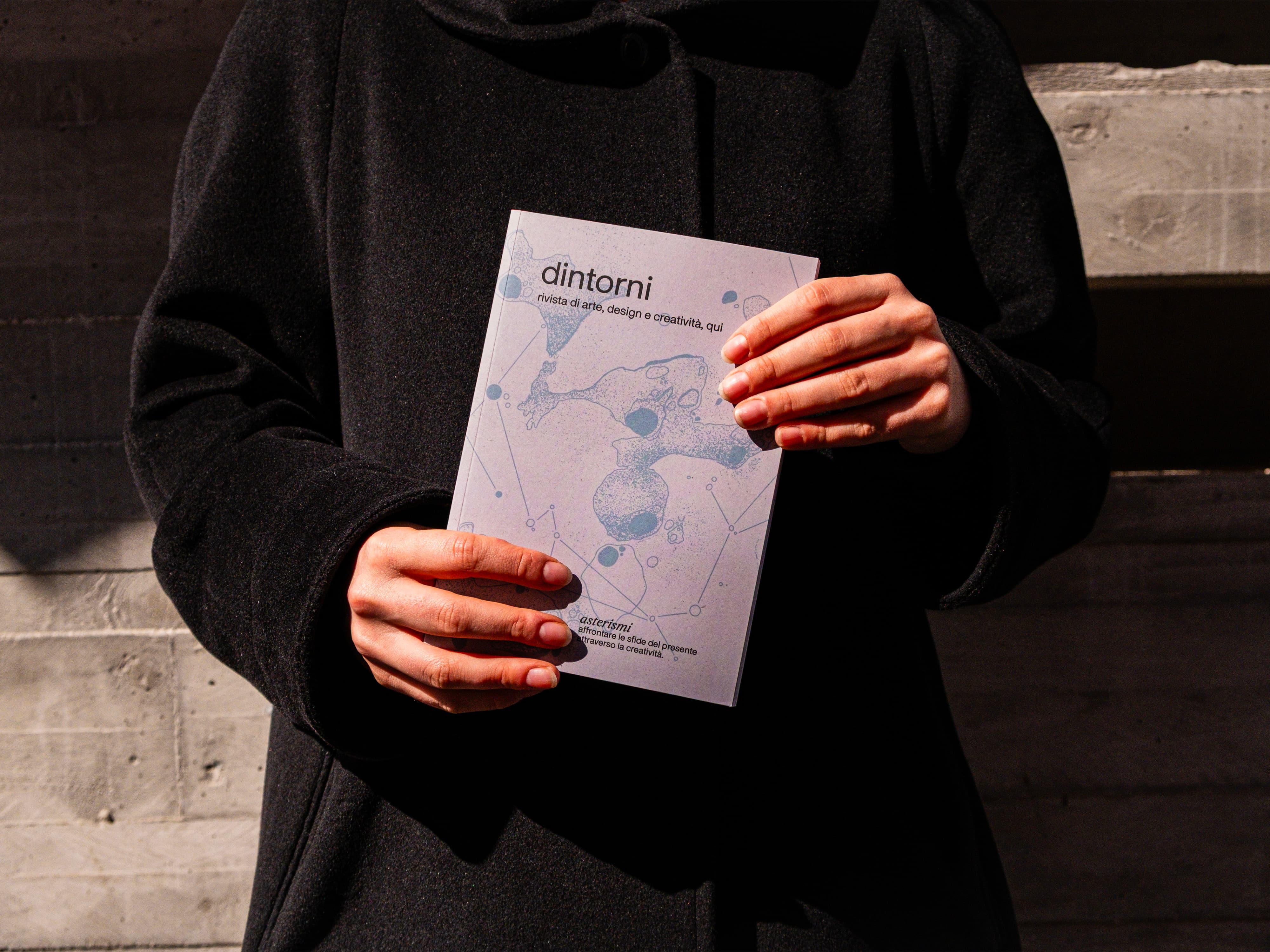 Person in a black jacket holding a pale Dintorni book.