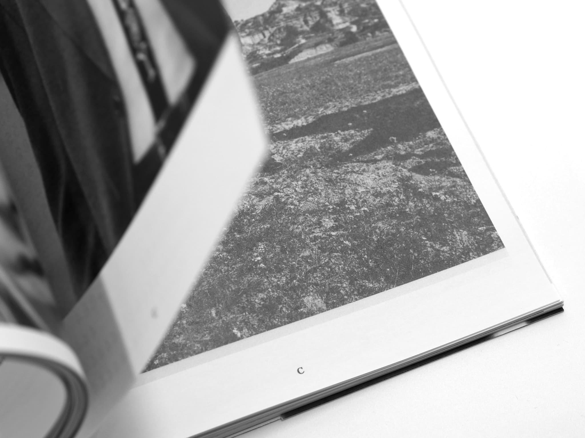 Close-up of an open Voltare pagina book showing a black-and-white photograph of textured ground.