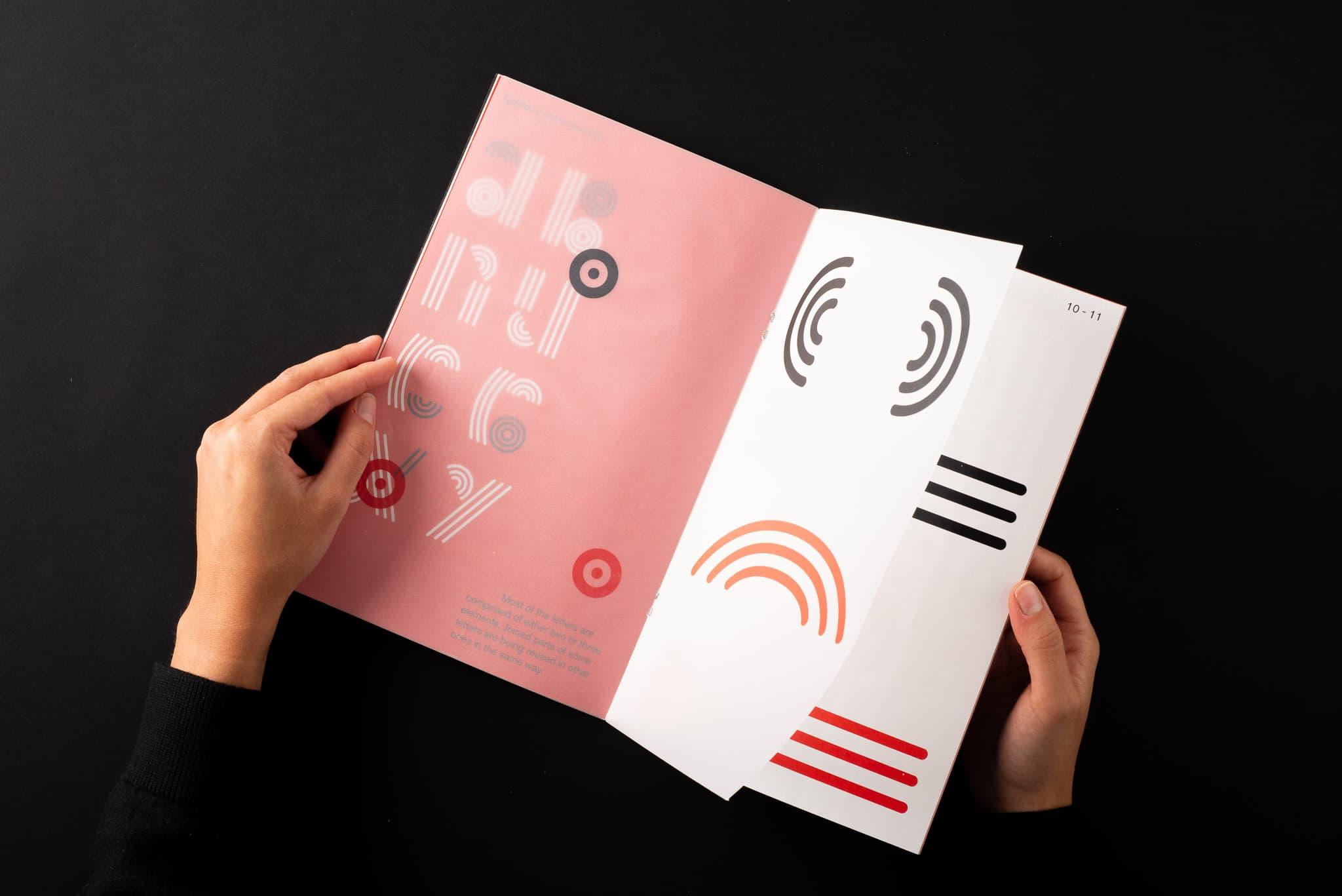 Hands holding an open Vinyl publication with pink and white pages.