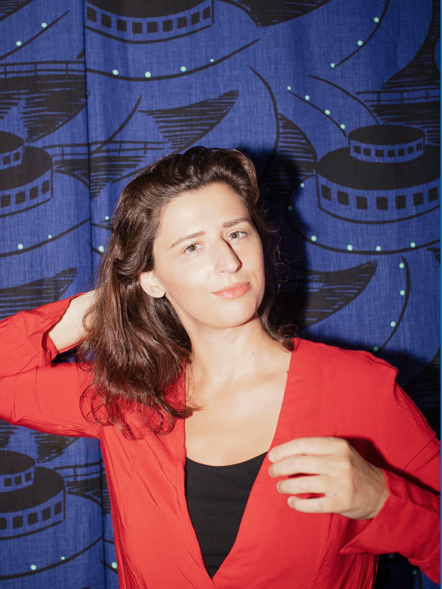 Portrait of a person in a red top in front of a blue patterned backdrop.
