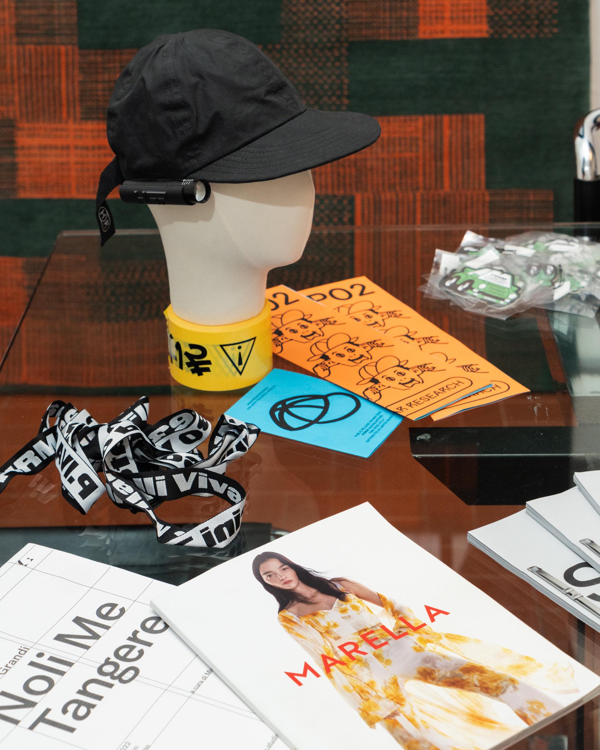 Design books, stickers and a mannequin head wearing a black cap on a glass table at Firm.