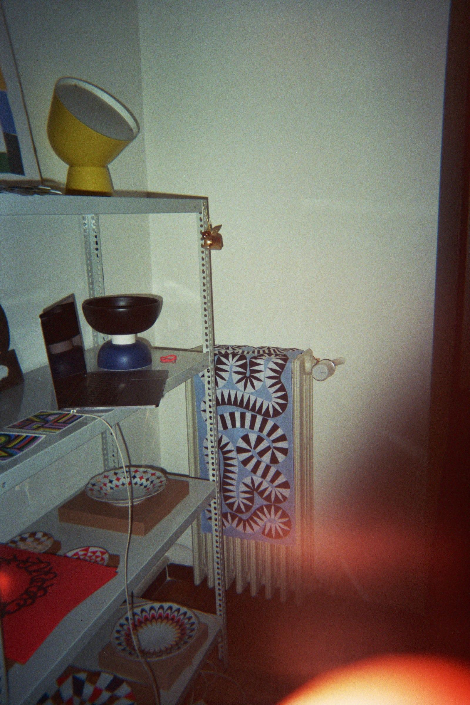 Studio shelf with lamps, ceramics and a patterned textile.