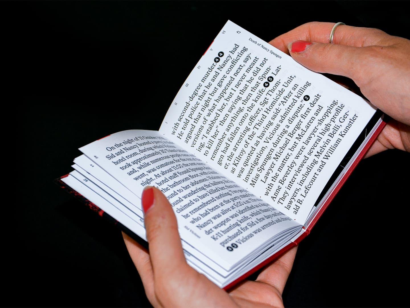 Hands holding an open No Future book with dense black text.