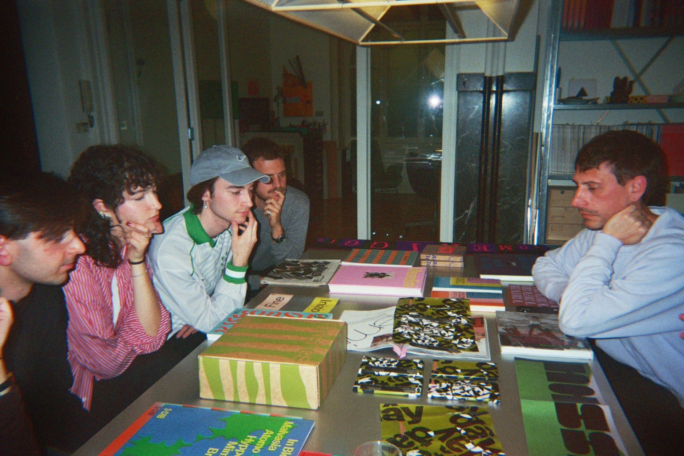 Attendees and hosts around a LaTigre worktable covered with books and printed work.