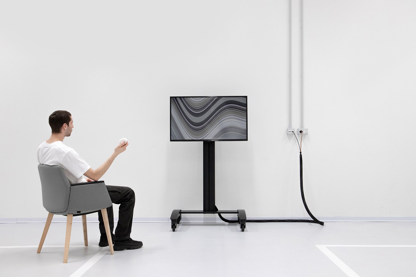 Person seated in a white room looking at a black screen on a stand.