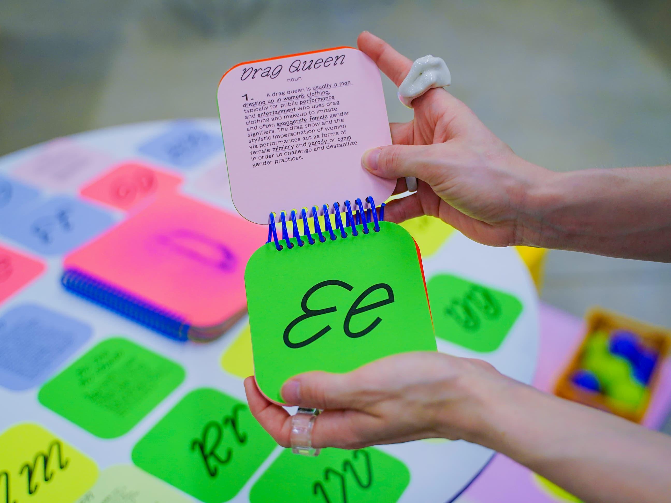 Hands holding small green and pink flip cards above a colourful board.