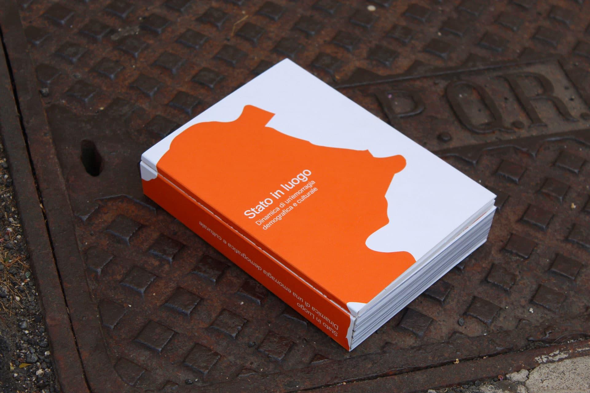Orange and white Stato in Luogo book on patterned metal flooring.