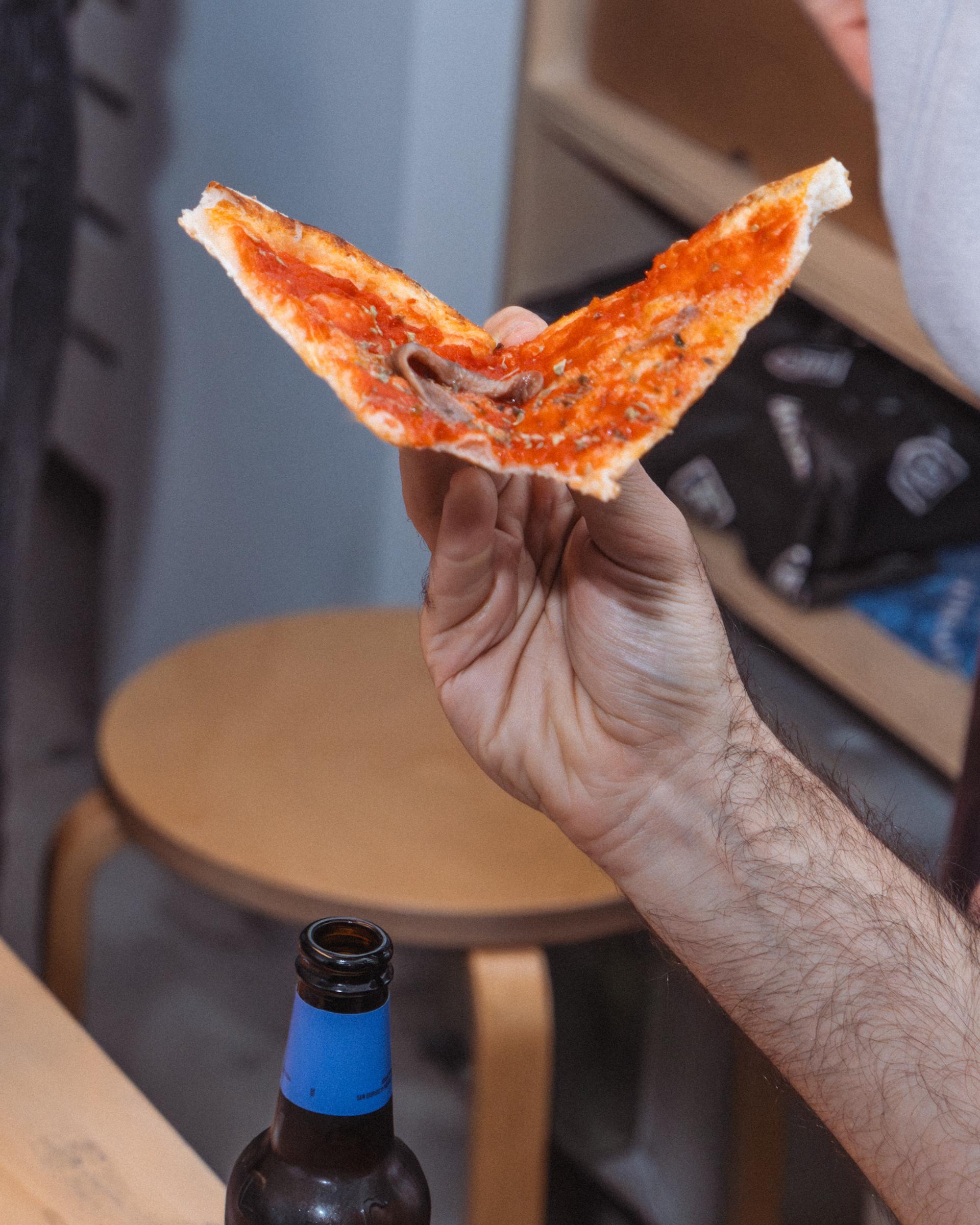 Hand holding a slice of pizza above a beer bottle.