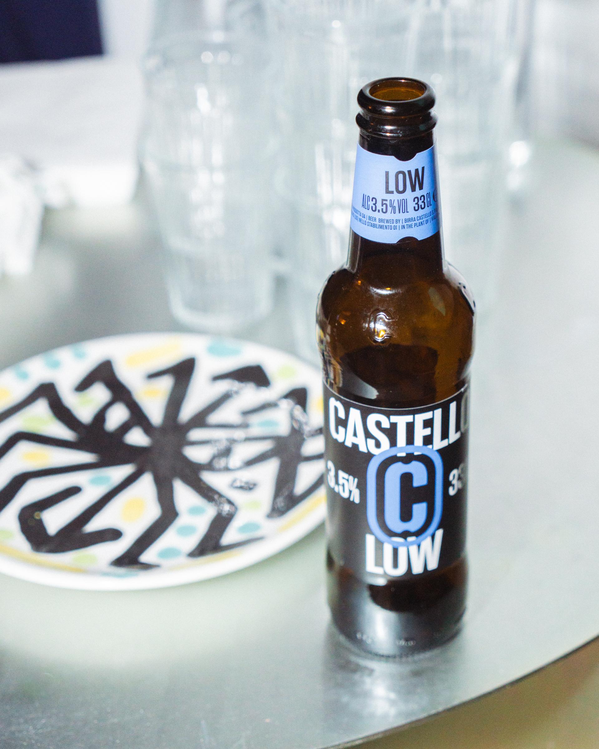 Castello Low beer bottle beside a plate with a black typographic drawing.
