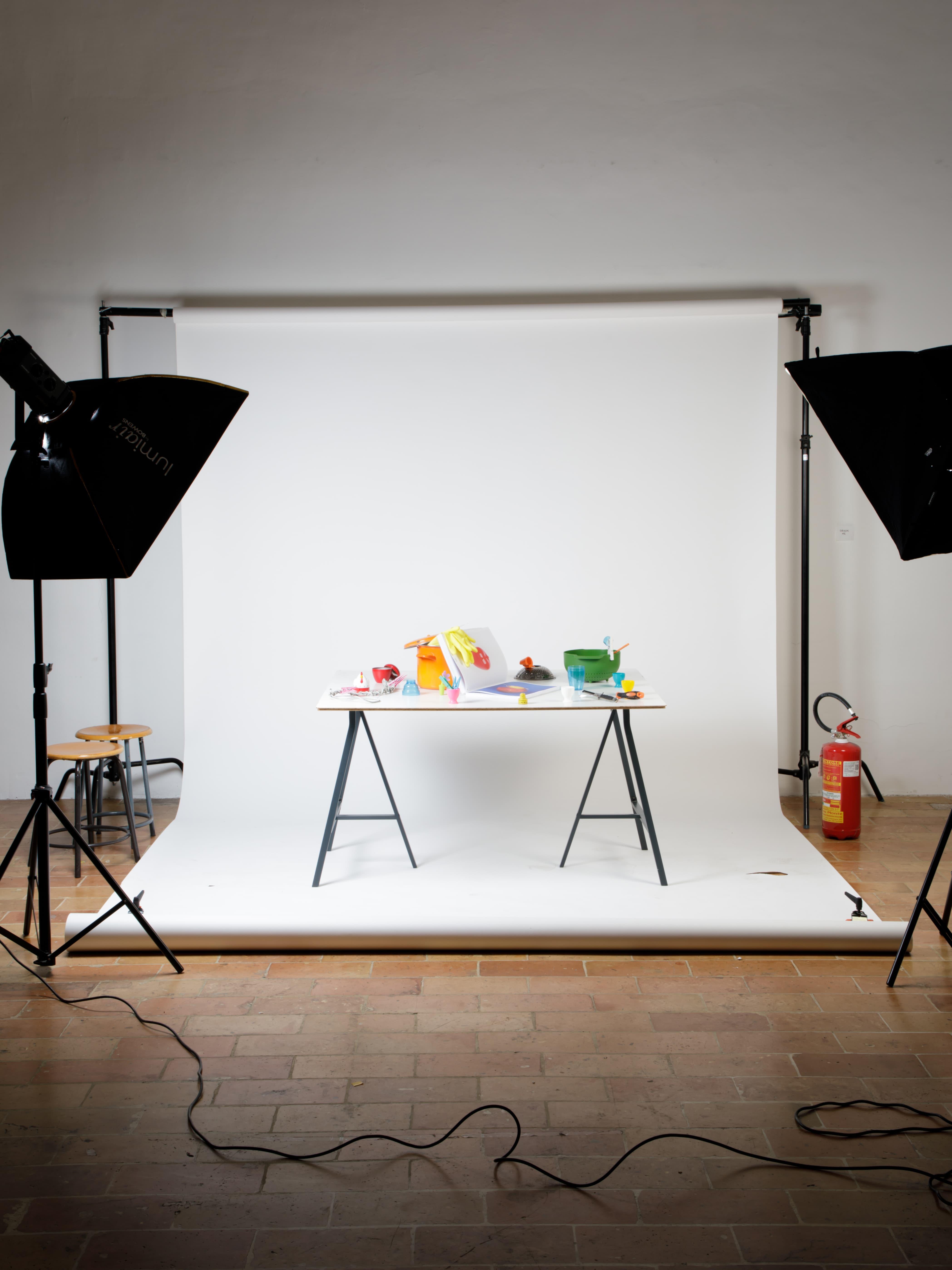 White studio with a table of colourful objects and softbox lights.