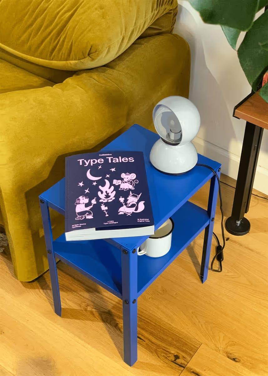 Type Tales font specimen book on a blue trolley beside a white lamp.